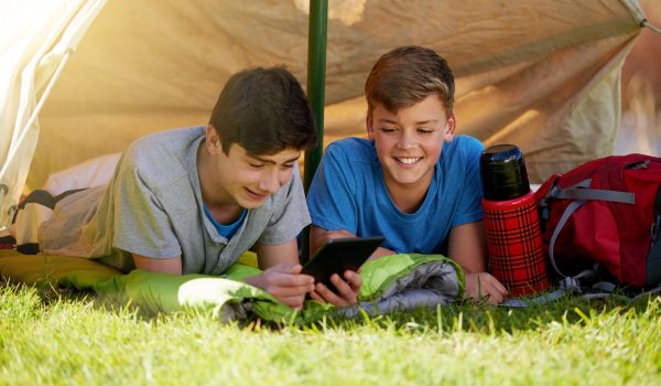 A young boy showing his friend something on a digital tablet while theyre camping